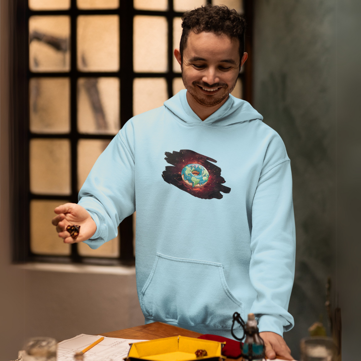 A young man rolls the dice tensely, wearing a light blue jumper with a donut surrounded by a galaxy depicted on it.