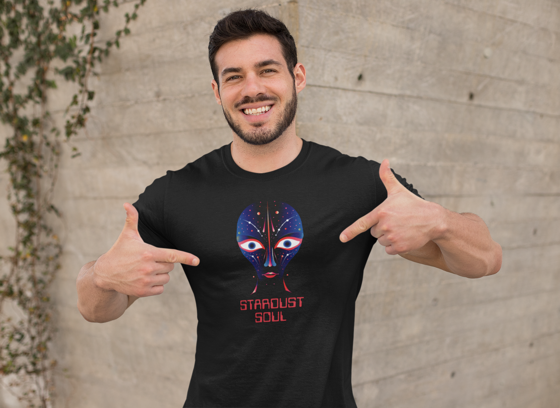 a sporty man smiles contentedly into the camera and points to his t-shirt, which has an alien print on it.