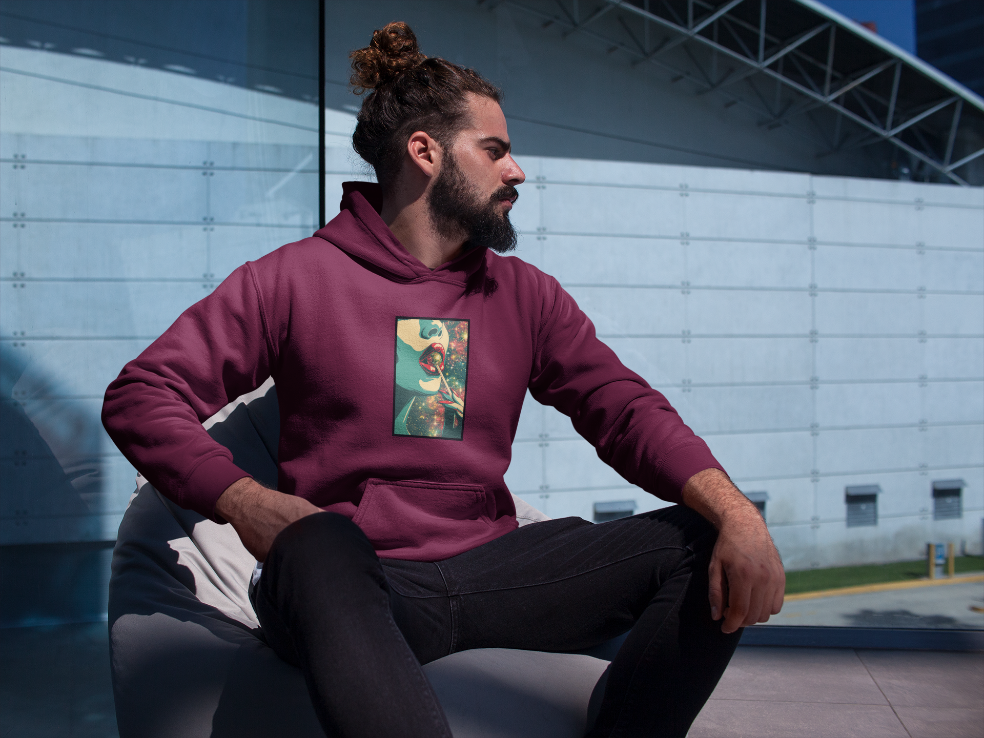 A man with a pigtail looks sideways into the distance wearing a red hoodie with a colourful galaxy print on it.